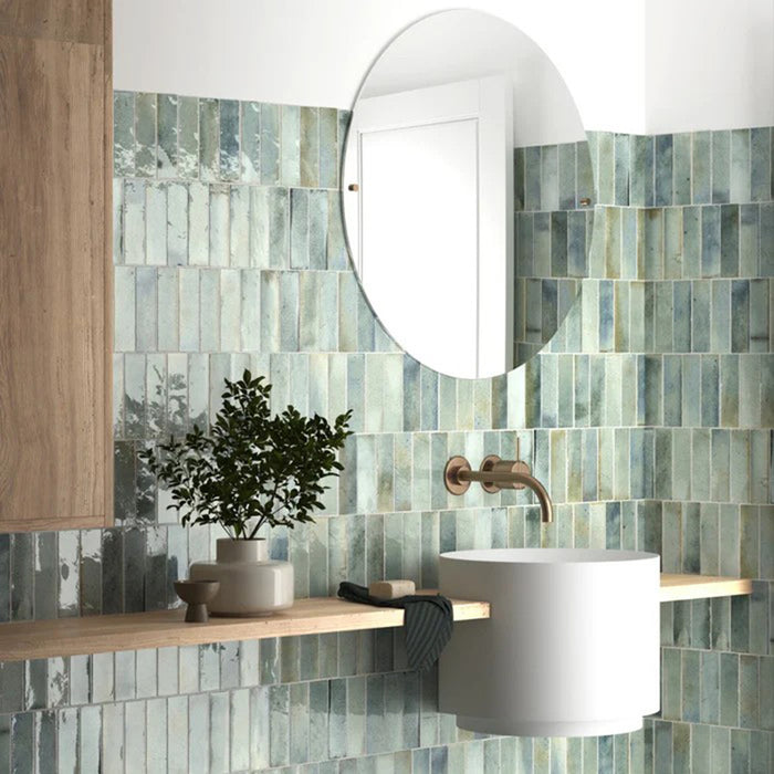 Bathroom wall featuring Saigon Celadon Green Brick Wall tiles in a Moroccan-inspired style, 5.1 × 16.1cm glossy ceramic tiles in soft green and blue tones, paired with a round mirror and minimalist vanity.