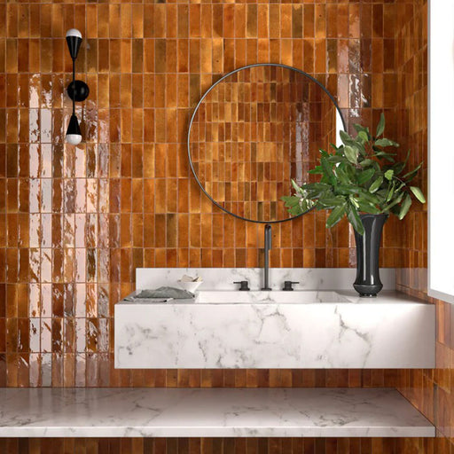 Bathroom wall featuring Saigon Amber Brick Wall tiles in a Moroccan-inspired style, 5.1 × 16.1cm glossy ceramic tiles in warm amber tones, paired with a marble vanity and round mirror.