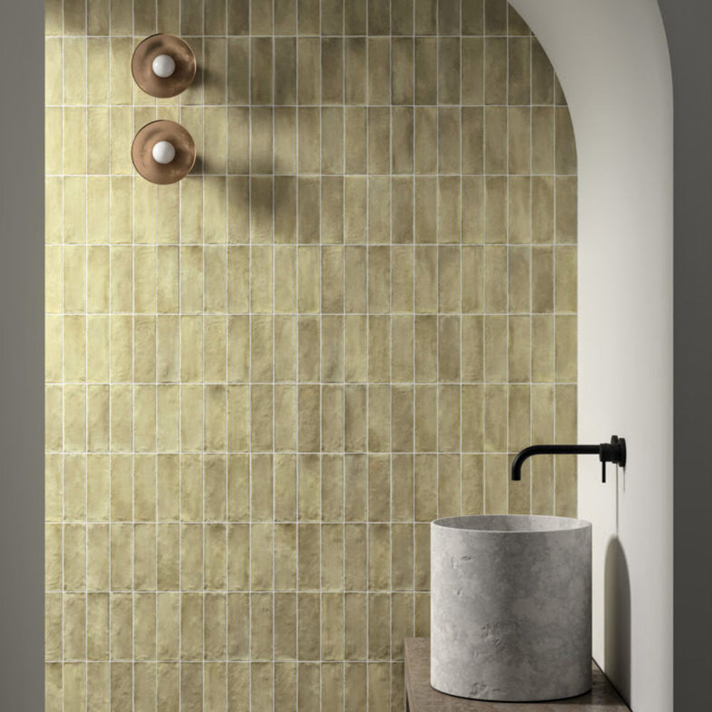 Bathroom featuring Zellige Weald Green 6.5×20cm Moroccan-style ceramic brick tiles installed on the walls within an arched shower area, showcasing soft green tonal variation, a handmade-look finish, and styled with minimalist concrete basin and matte black tapware.