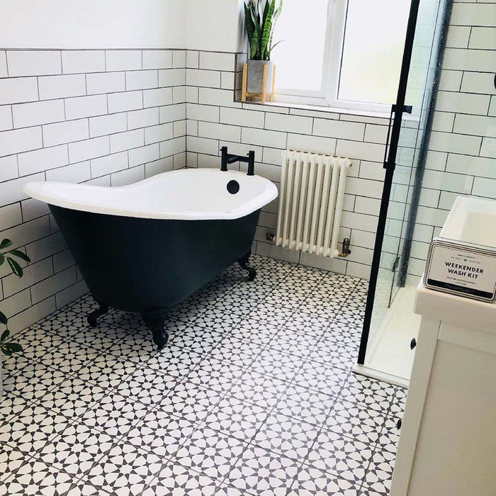 Bathroom setting featuring Agadir Black & White Moroccan-style 20x20cm porcelain floor tiles, showcasing a bold geometric star pattern, styled with a freestanding bath, white metro wall tiles and black fittings.