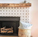 Agadir Silver Moroccan-style 20x20cm porcelain tiles used to frame a fireplace, featuring a soft grey geometric pattern paired with a rustic wooden mantel and neutral accessories for a warm, contemporary living space.