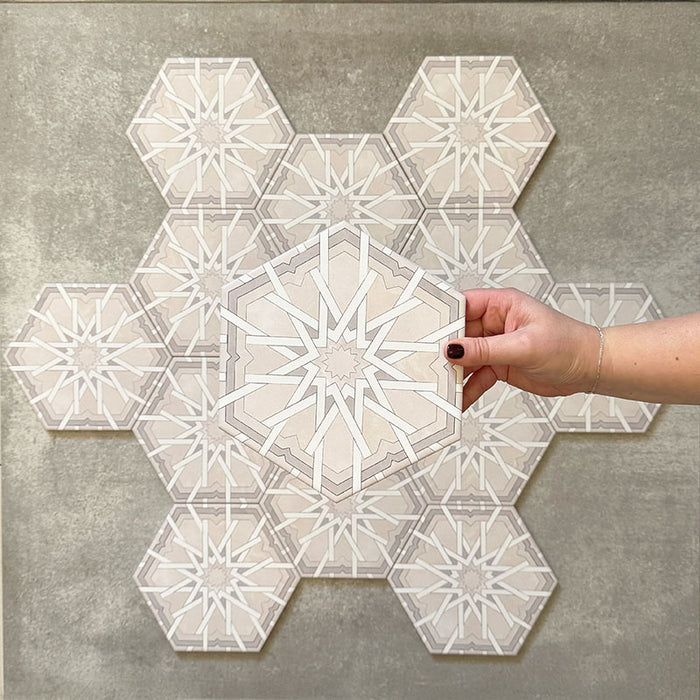 Hand holding Medina Hormuz Snow White Moroccan-style hexagon porcelain tile, 18.7 × 21.6 cm, shown against a grouped layout to highlight the crisp star-inspired geometric pattern in white and soft grey tones.