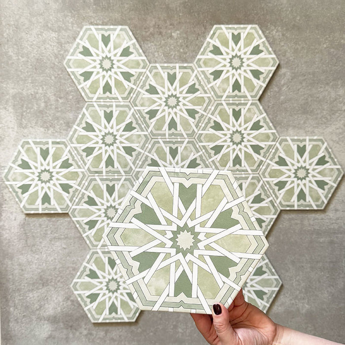 Hand holding Medina Hormuz Verde Green Moroccan-style hexagon porcelain tile, 18.7 × 21.6 cm, shown against a grouped layout to highlight the bold star-patterned design in green and white tones.