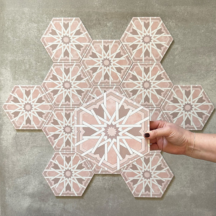 Hand holding Medina Hormuz Rose Moroccan-style hexagon porcelain tile, 18.7 × 21.6 cm, shown against a grouped layout to highlight the bold star-inspired geometric pattern in soft rose and white tones.