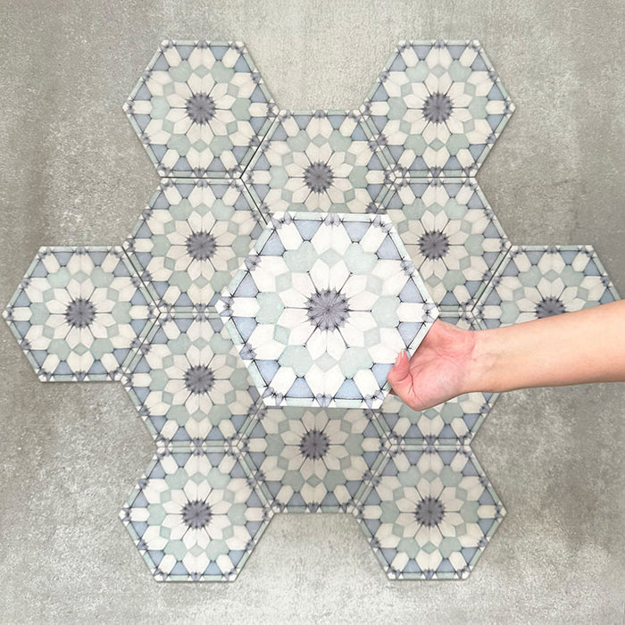 Hand holding Medina Frost Blue Moroccan-style hexagon porcelain tile, 18.7 × 21.6 cm, shown against a grouped layout to highlight the repeating geometric pattern in soft blue and white tones.