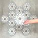 Hand holding Medina Frost Blue Moroccan-style hexagon porcelain tile, 18.7 × 21.6 cm, shown against a grouped layout to highlight the repeating geometric pattern in soft blue and white tones.