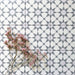 Agadir Silver Moroccan-style 20x20cm porcelain tiles arranged in a repeating geometric pattern, shown as a group layout with soft grey detailing and delicate pink flowers for a calm, contemporary look.