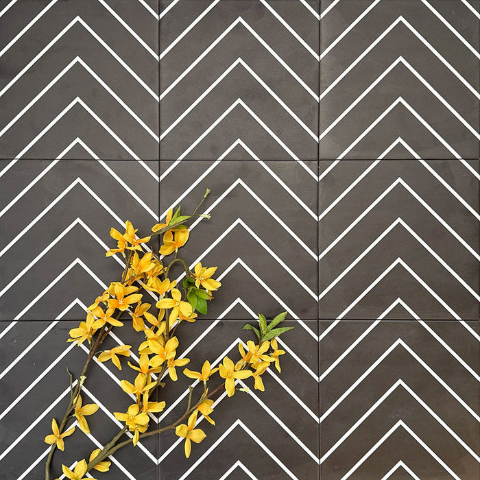 Grouped Almeria Jilani Black Moroccan-style porcelain wall and floor tiles arranged in a repeating white line chevron pattern, 20x20cm, styled with yellow florals to highlight the geometric design.