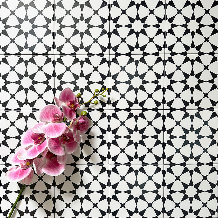 Agadir Black & White Mini Moroccan-style 15x15cm porcelain floor tiles laid in a repeating geometric star pattern, styled with a decorative orchid to highlight the bold black and white design.