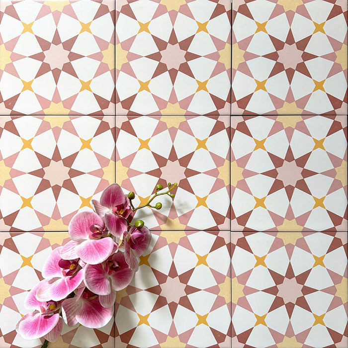 Agadir Springs Moroccan-style 20x20cm porcelain floor tiles laid in a repeating geometric star pattern, showcasing soft terracotta, blush pink, white and warm yellow tones, styled with a decorative orchid for a warm, inviting look.