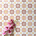 Agadir Springs Moroccan-style 20x20cm porcelain floor tiles laid in a repeating geometric star pattern, showcasing soft terracotta, blush pink, white and warm yellow tones, styled with a decorative orchid for a warm, inviting look.