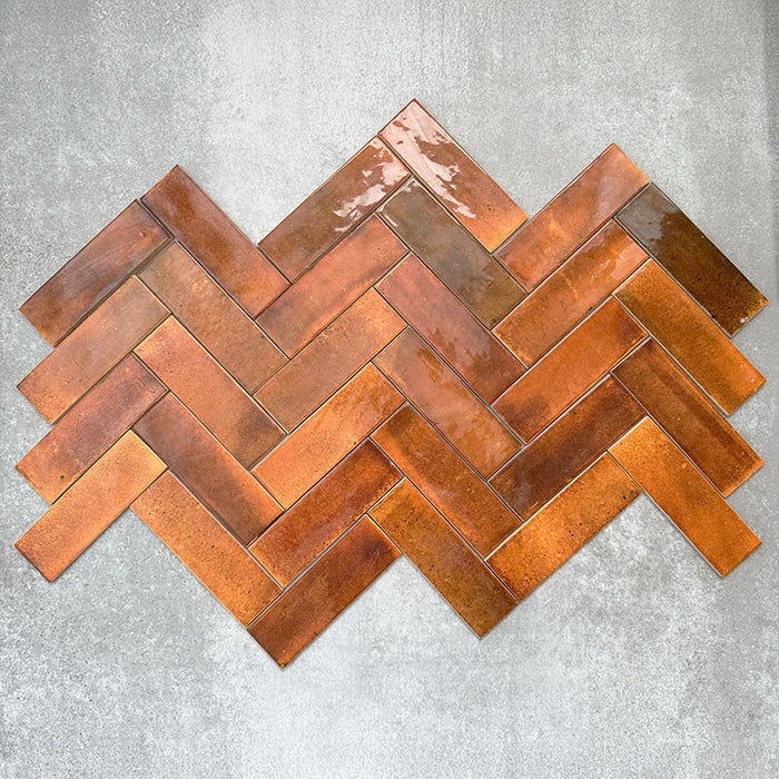 Saigon Amber Brick Wall tiles laid in a herringbone pattern, showcasing Moroccan-style 5.1 × 16.1cm glossy ceramic tiles with warm amber and copper-toned variation.