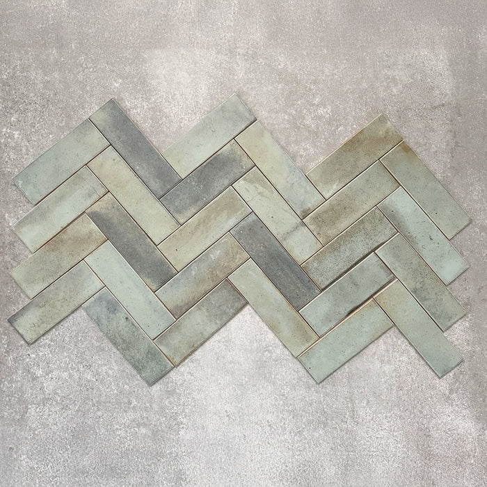 Saigon Celadon Green Brick Wall tiles laid in a herringbone pattern, showcasing Moroccan-style 5.1 × 16.1cm glossy ceramic tiles with soft green and blue-grey tonal variation.