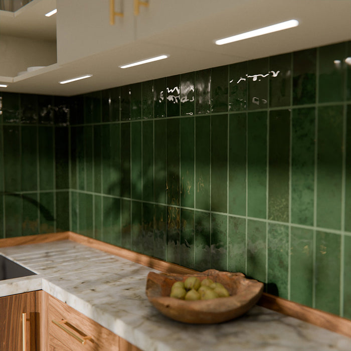 Gloss moss green Nairobi handmade-effect tiles shown in a kitchen setting, highlighting the rich colour depth and lightly textured glazed surface alongside natural wood units and brass details.