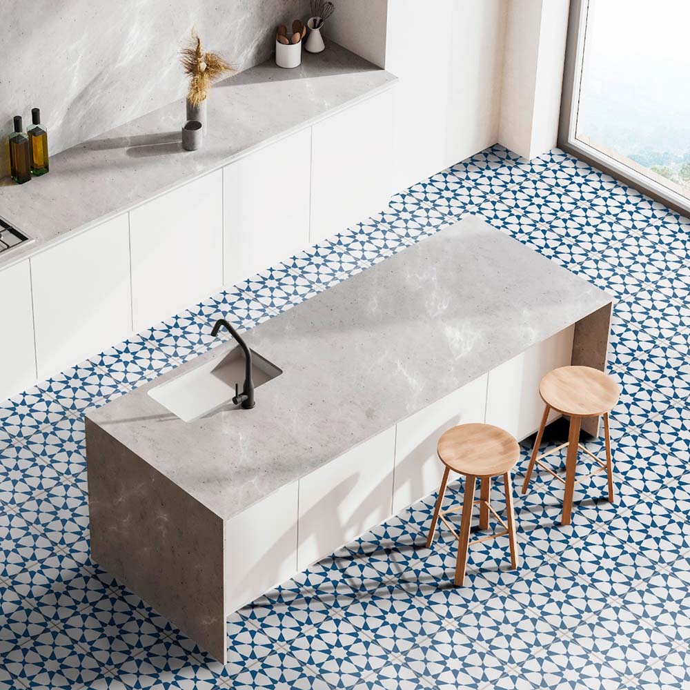 Kitchen interior featuring Agadir Navy Blue Moroccan-style 20x20cm porcelain floor tiles, displaying a geometric star pattern in navy and white, styled with a modern island, concrete worktop and wooden stools.