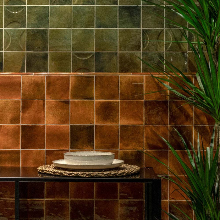 Interior detail featuring Saigon Amber Square Wall tiles in a Moroccan-inspired style, 10 × 10cm glossy ceramic tiles in warm amber tones, styled with layered tiles, greenery, and decorative tableware.