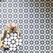 Marketing image featuring Agadir Black & White Moroccan-style 20x20cm porcelain floor tiles laid in a repeating geometric star pattern, styled with decorative accessories to highlight the bold black and white design.