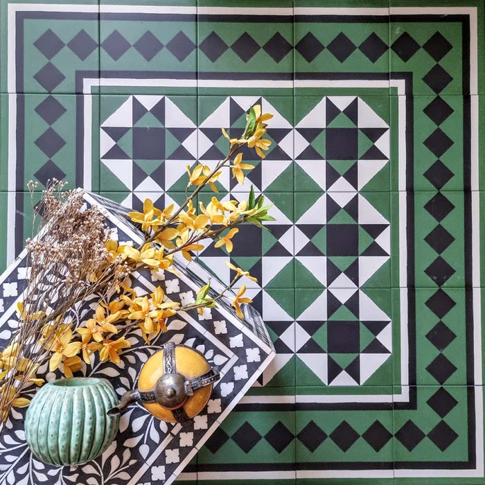 Styled flat lay of Greenbrook Manor anti-slip encaustic Victorian-style porcelain tiles, showcasing a green, black and white geometric pattern with decorative border tiles, accented with dried flowers and ceramic accessories.