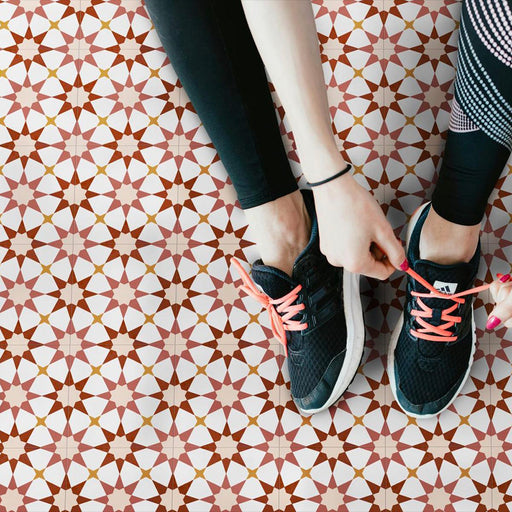 Marketing image featuring Agadir Cotto Moroccan-style 20x20cm porcelain floor tiles laid in a repeating geometric star pattern in warm terracotta, white and soft yellow tones, styled with trainers to highlight durability and everyday use.
