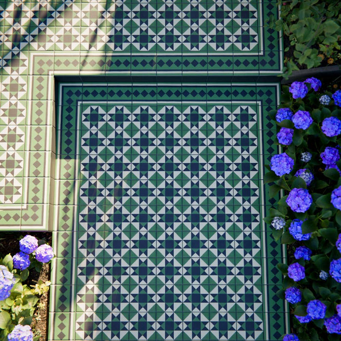 Greenbrook Manor side/border 20cm x 20cm porcelain tiles used to create a green, black and white Victorian-style geometric border framing a patterned outdoor pathway, surrounded by planting and blue flowers.