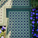 Top-down view of an outdoor tiled area using Greenbrook Manor anti-slip encaustic Victorian-style porcelain tiles, featuring a green, black and white geometric pattern framed with decorative border tiles and bordered by flowering plants.