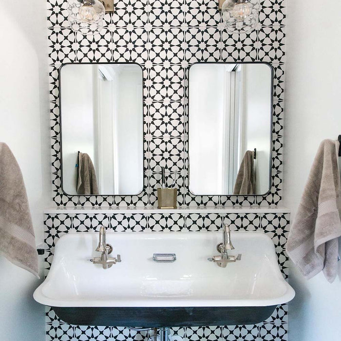 Bathroom sink area featuring Agadir Black & White Mini Moroccan-style 15x15cm porcelain wall tiles, showcasing a bold geometric star pattern, styled with twin mirrors, a classic basin and chrome taps.